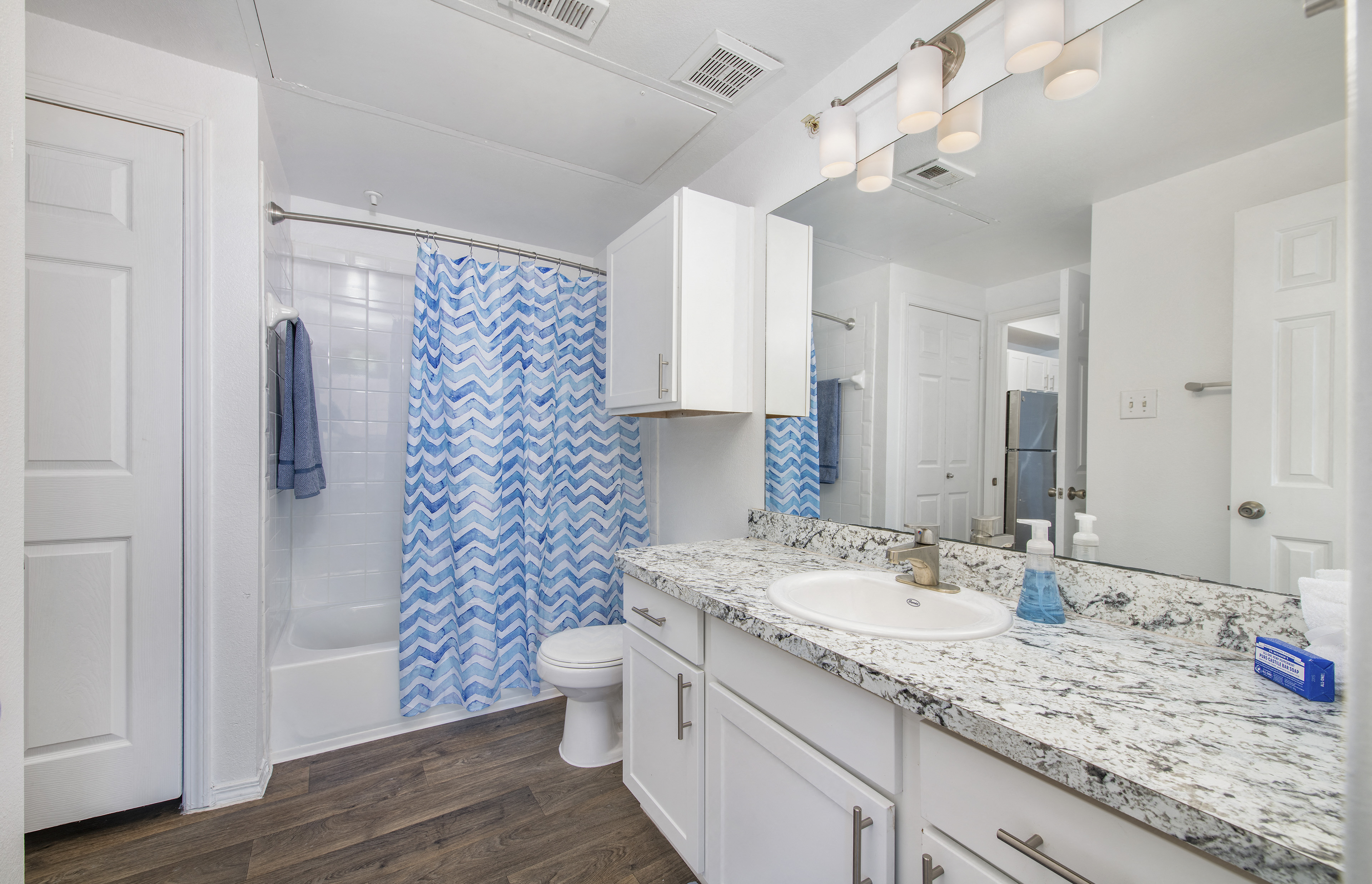 a bathroom with white cabinets and a blue and white shower