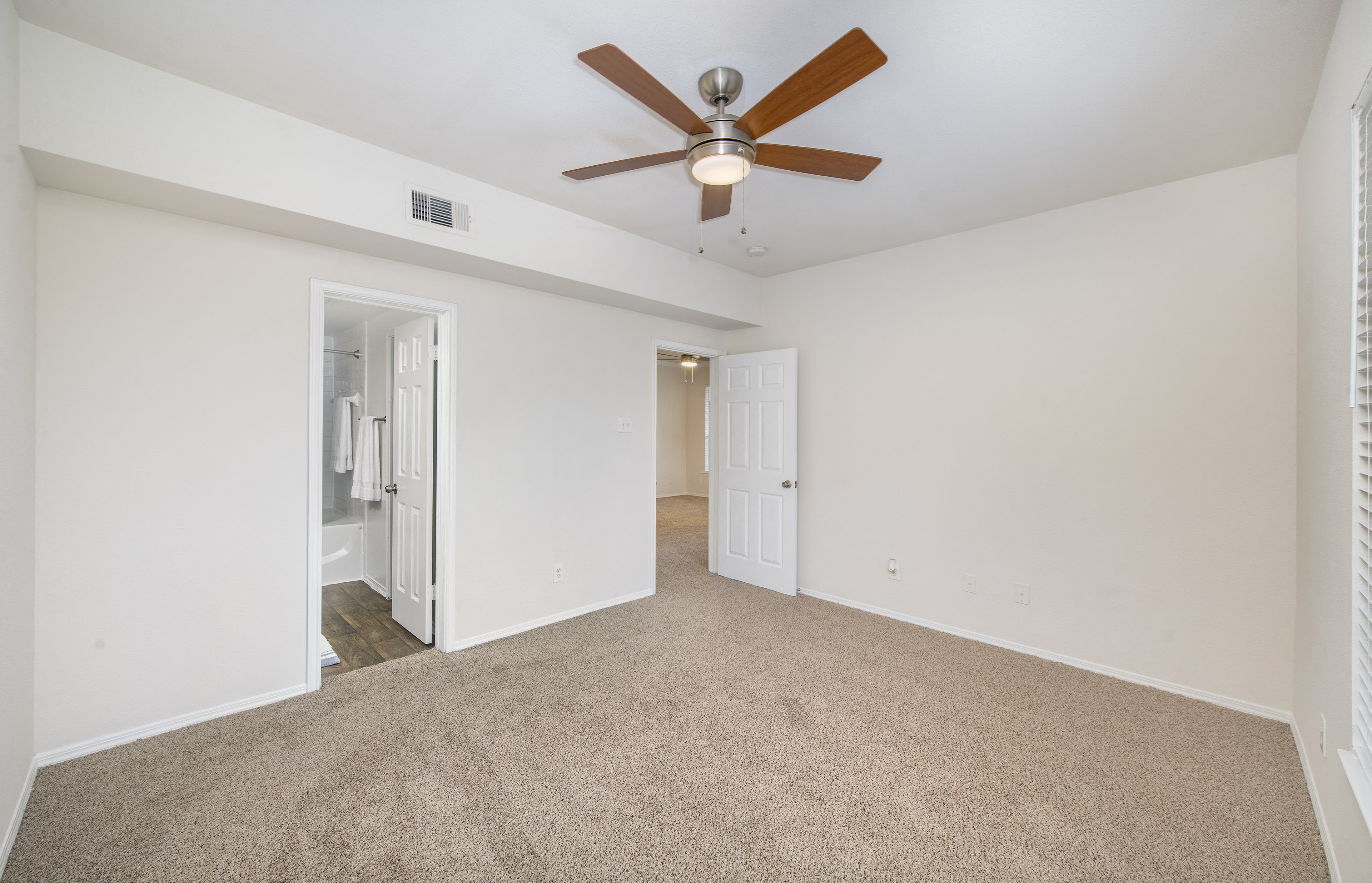 a spacious living room with carpet and a ceiling fan