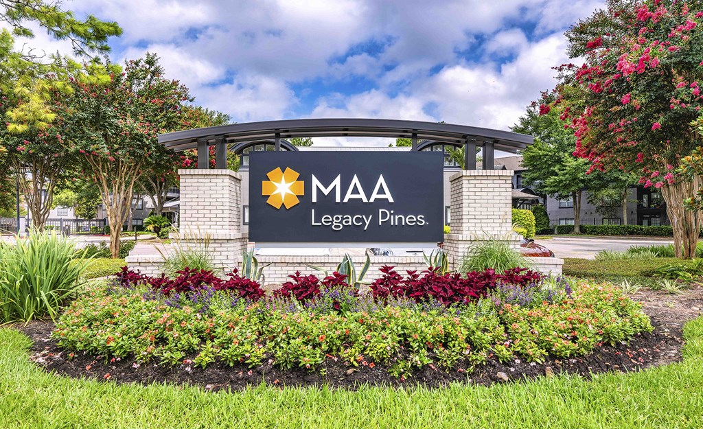 a sign for mgm legacy pines in front of a park with flowers