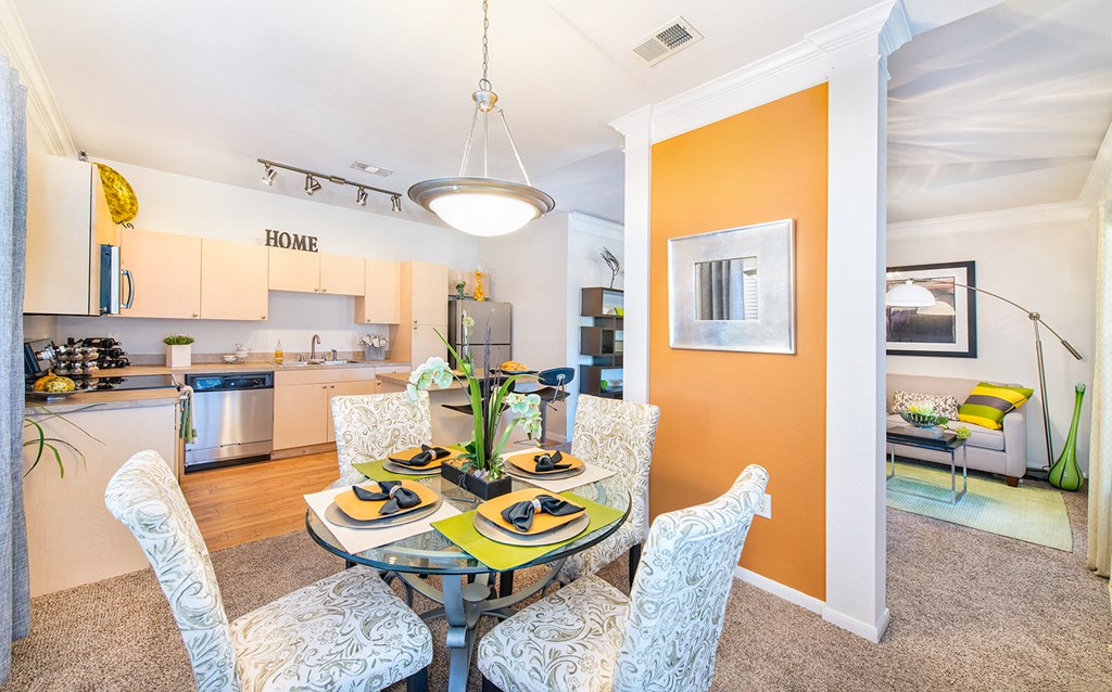 a dining area with a table and chairs and a kitchen in the background