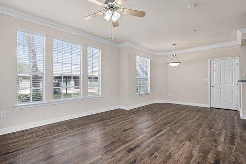 an empty living room with a ceiling fan and windows