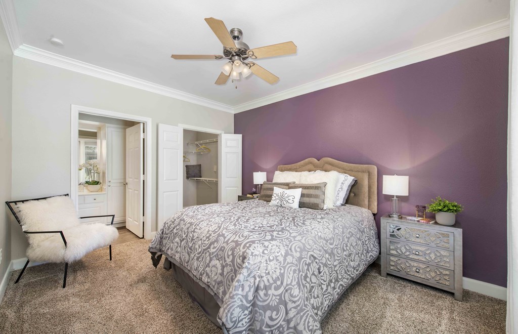 A bedroom with a bed, chair, and ceiling fan.