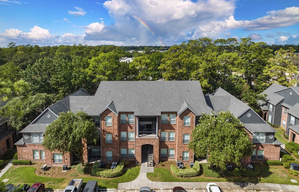 A large brick house with a grey roof and a green tree in front.