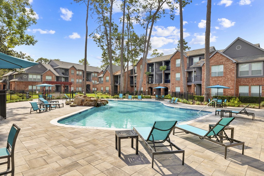A pool surrounded by chairs and trees in front of apartment buildings.