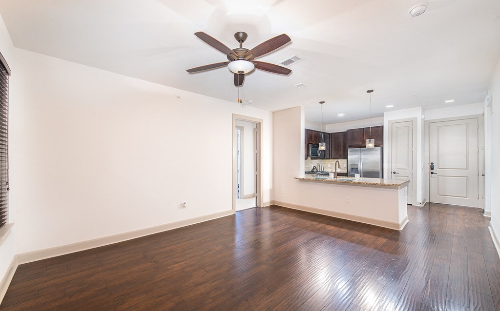 an empty living room with a ceiling fan and a kitchen