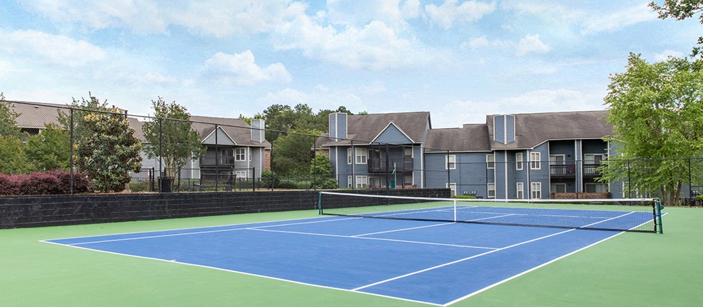 a blue and green tennis court with apartments in the background