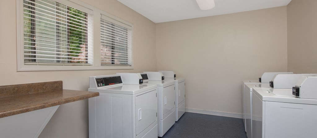 a laundry room with four washers and dryers and a window