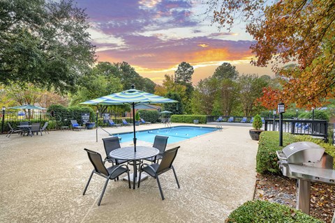 A poolside table with chairs and an umbrella overlooking a pool.