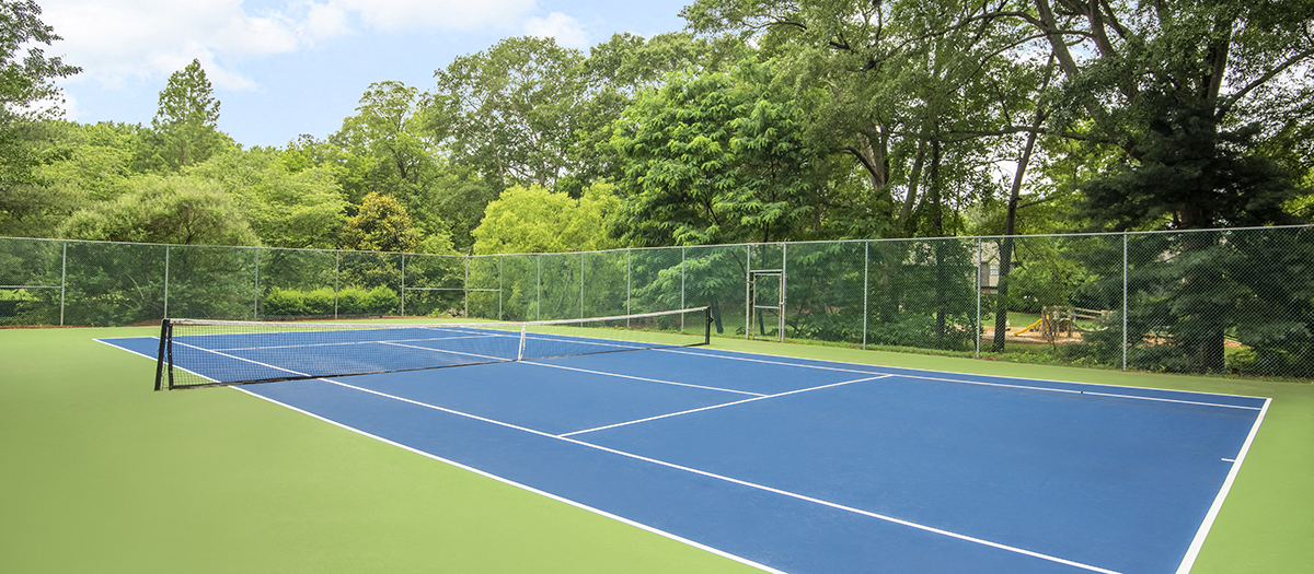 a blue and green tennis court with a fence and trees