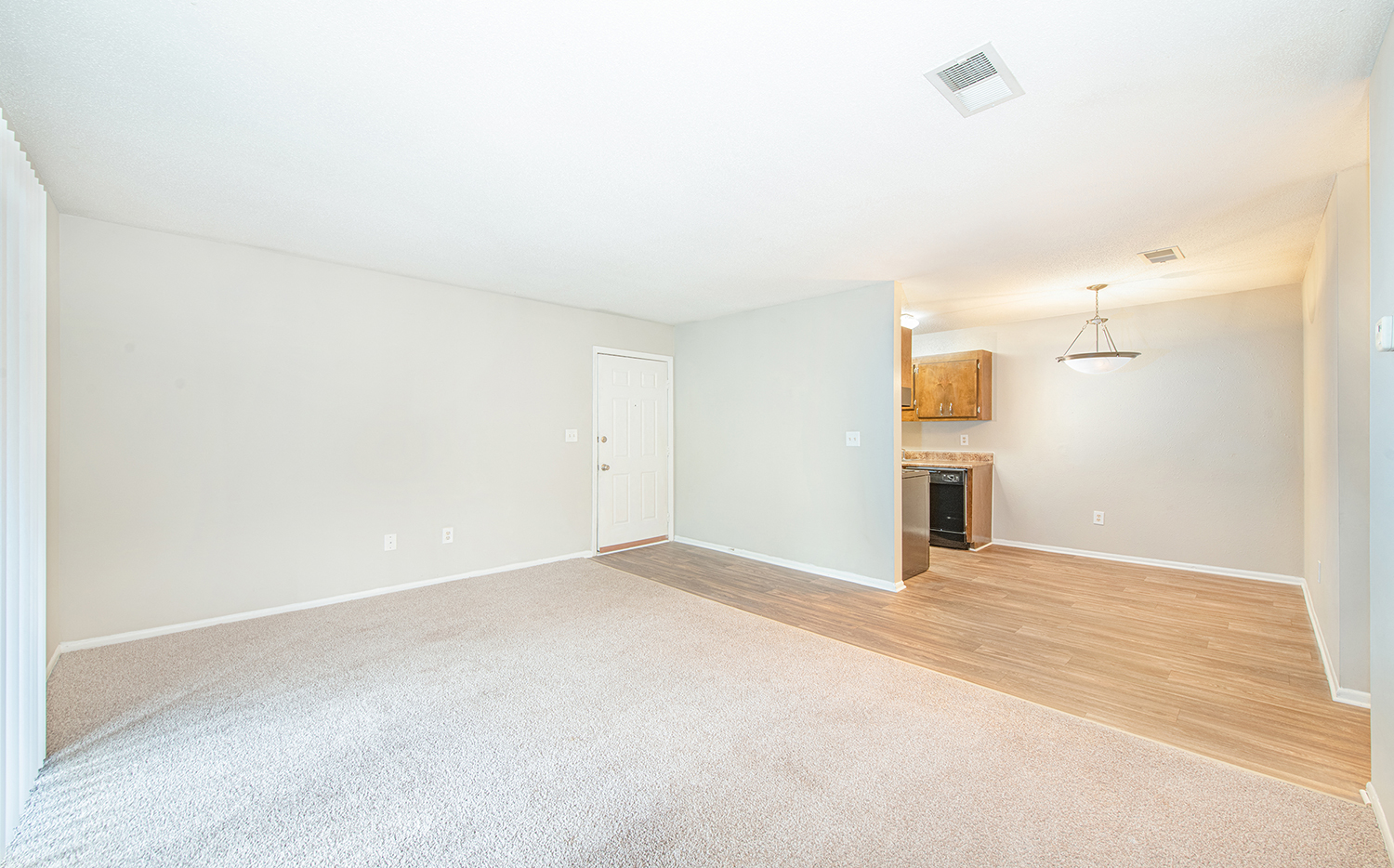 an empty living room with wood flooring and a kitchen