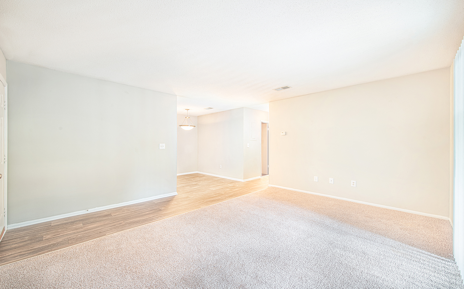 the living room and dining room of an apartment with carpet and white walls