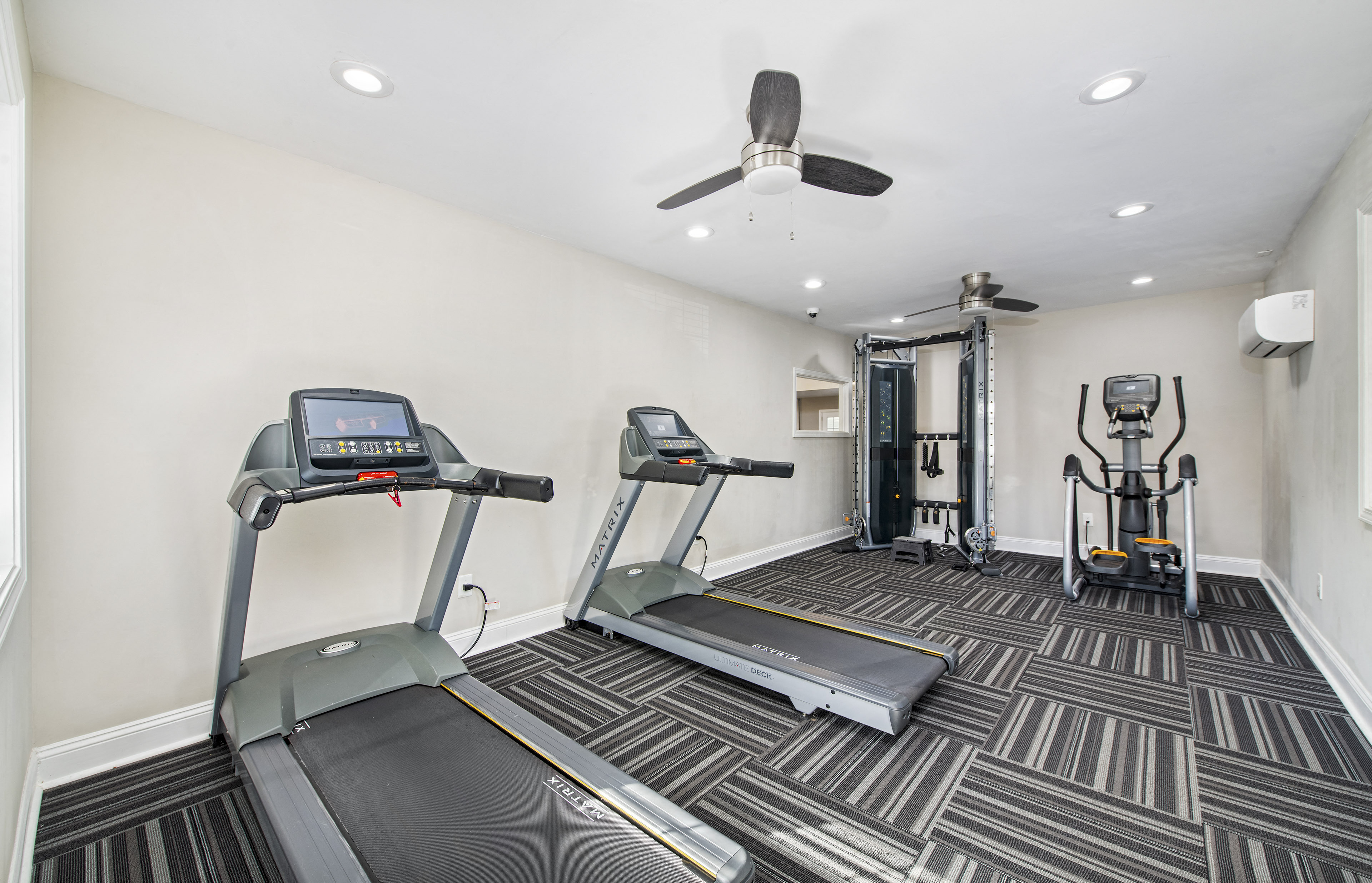 two treadmills and other exercise equipment in a gym with a ceiling fan