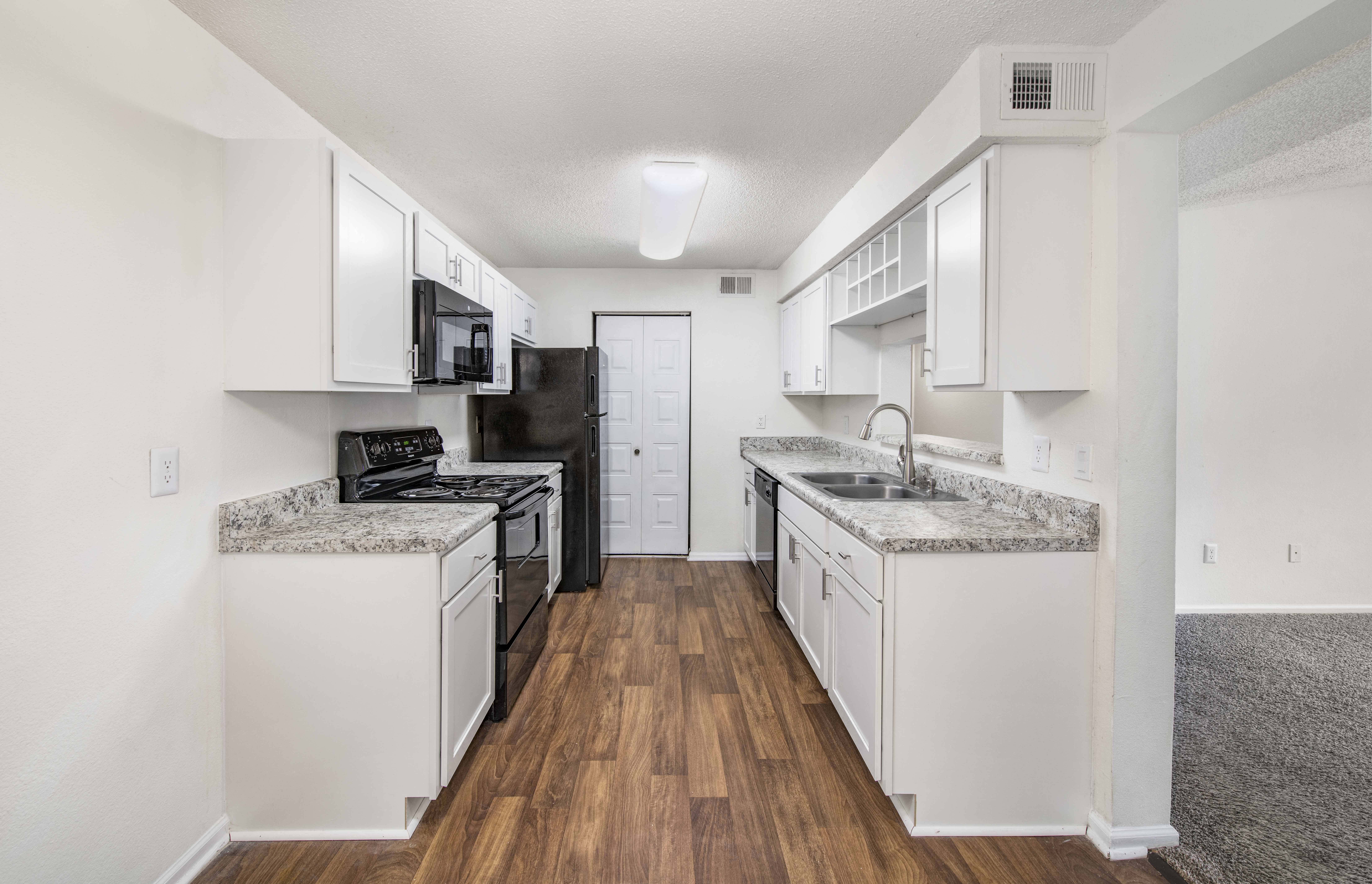 a spacious kitchen with white cabinets and white appliances and wood flooring