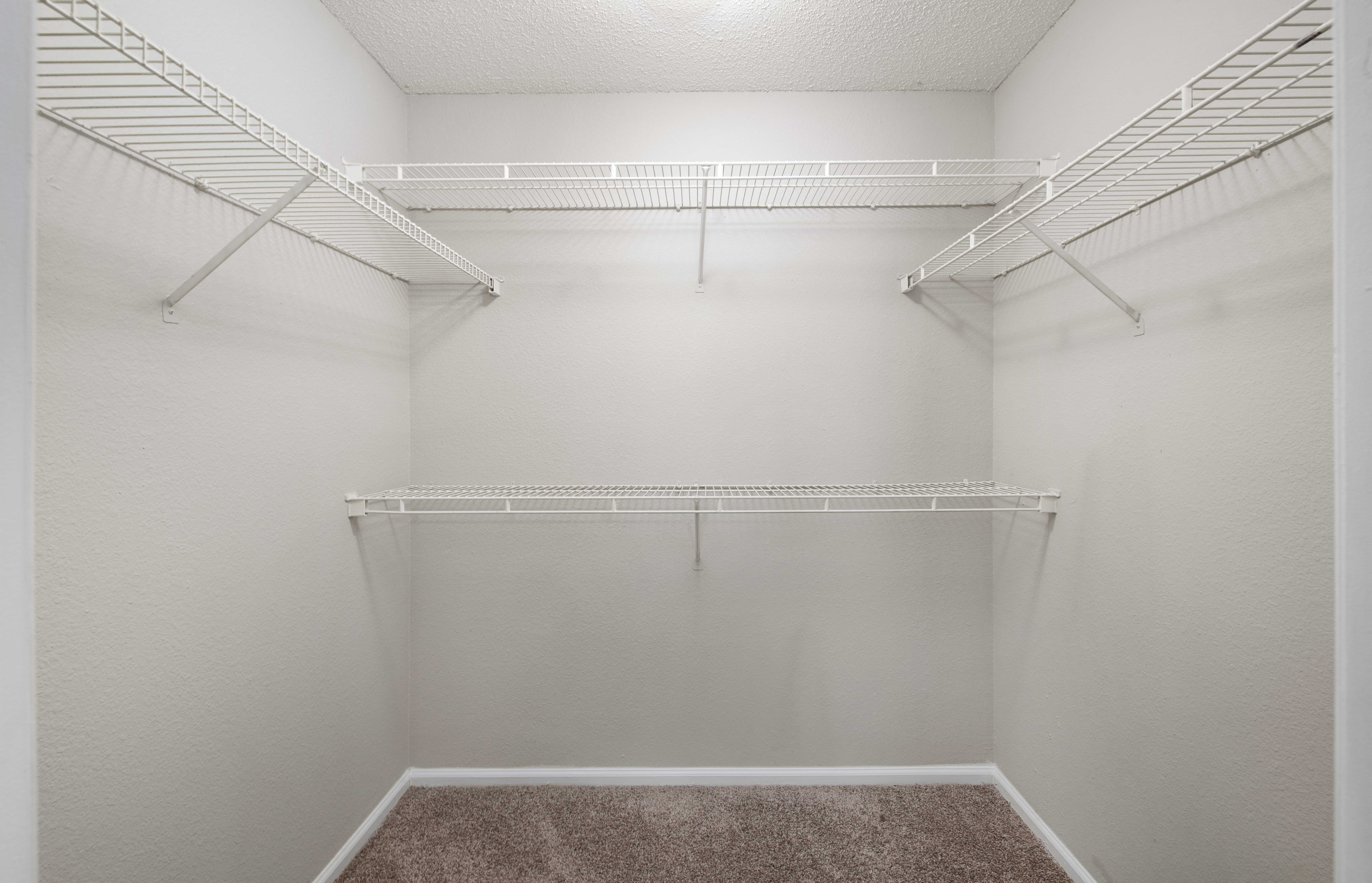 a spacious walk in closet with white walls and empty shelves