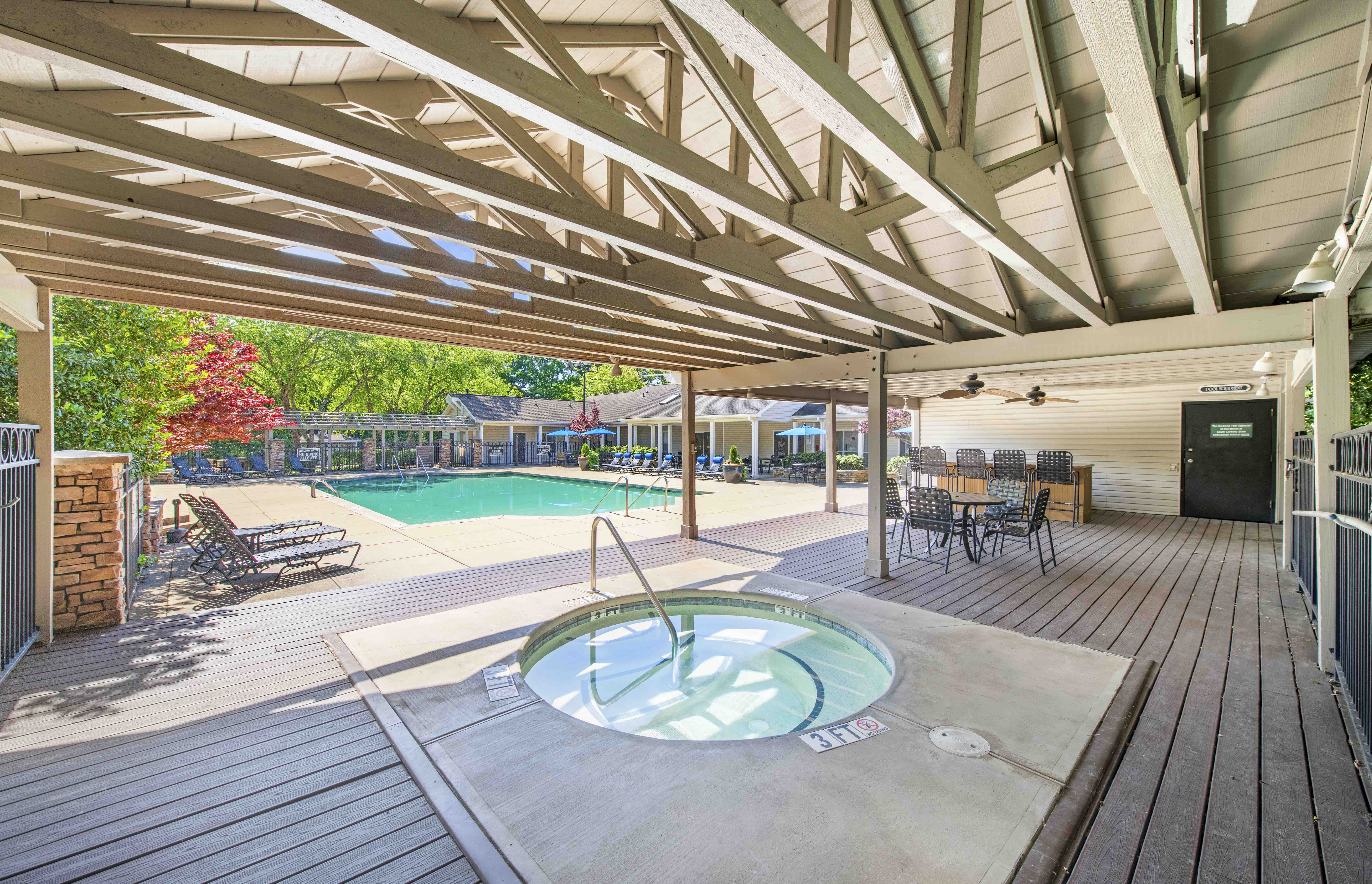 a pool with a hot tub and a poolside deck with chairs and a patio