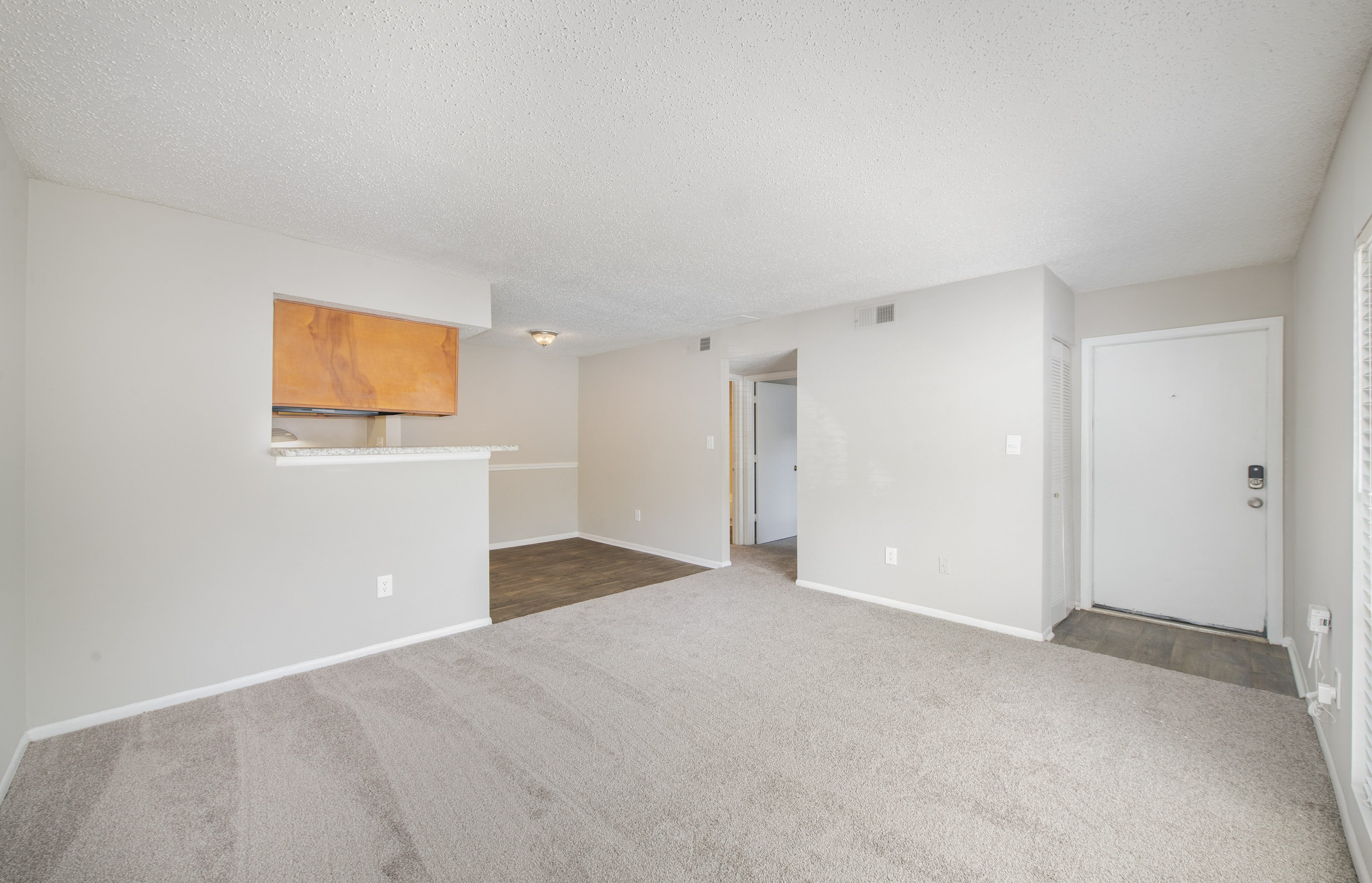the living room and kitchen of an apartment with white walls and carpet