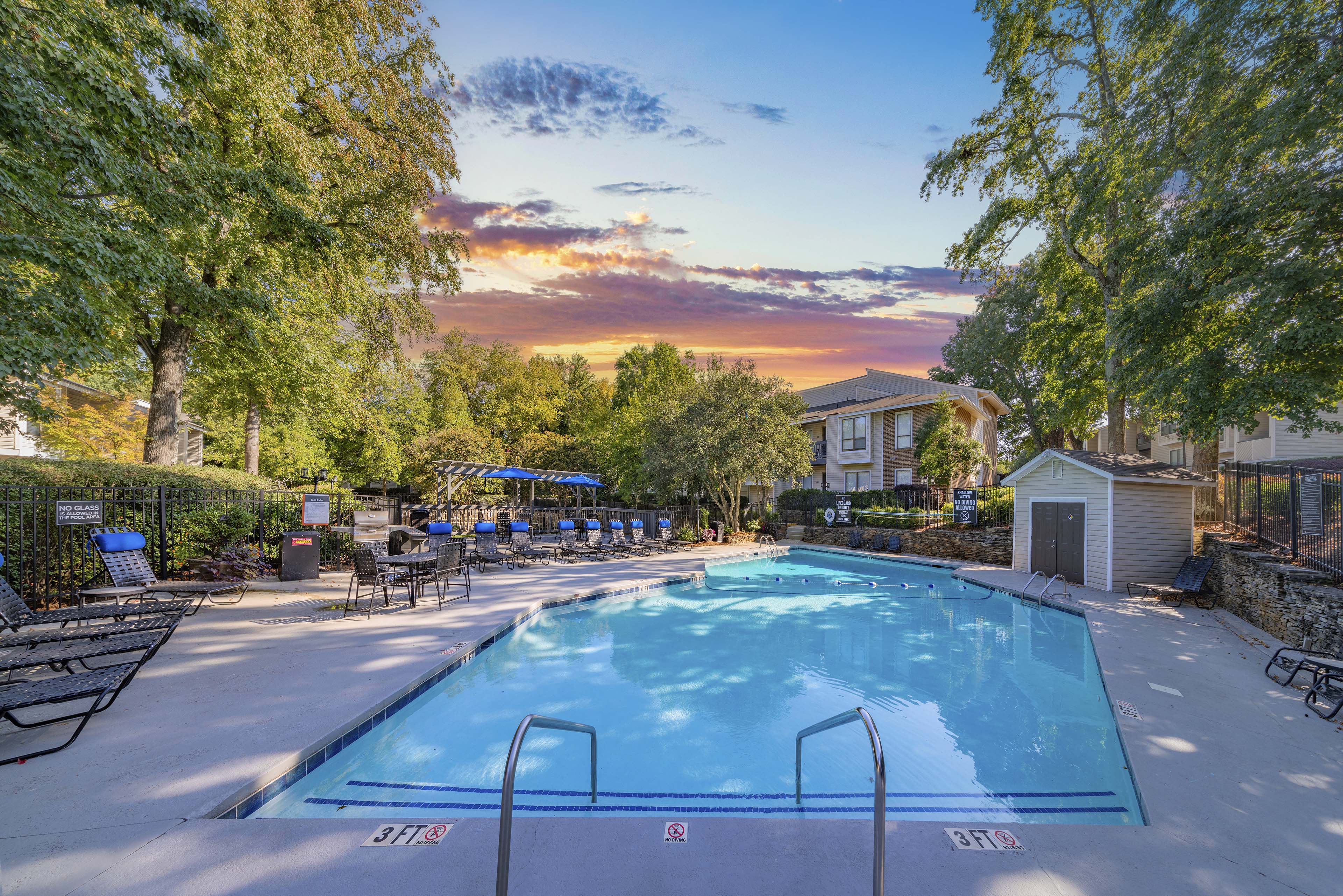 a swimming pool with trees and a sunset over the pool