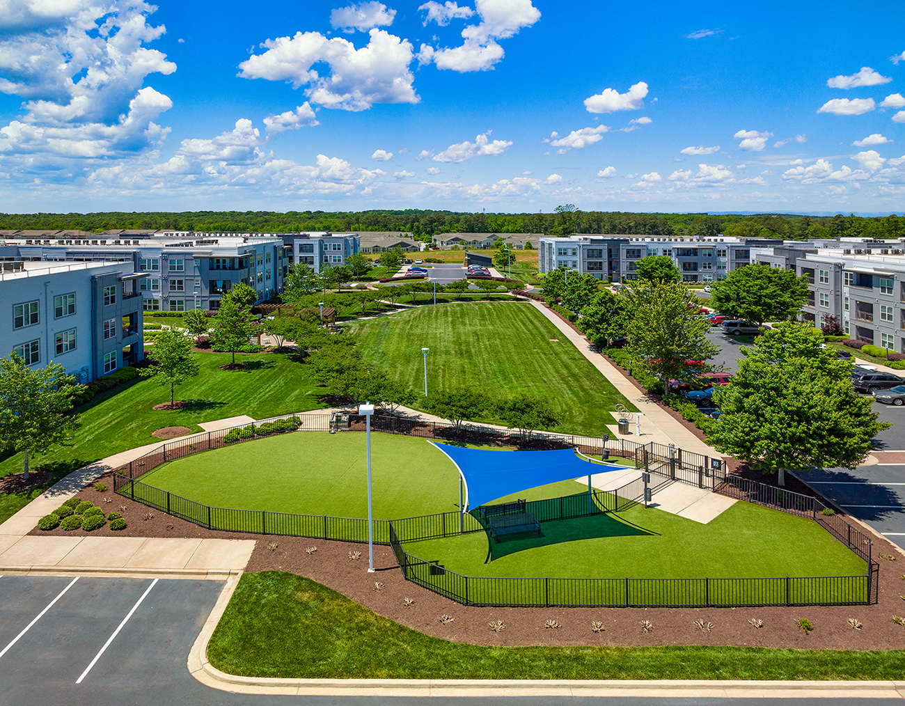 an aerial view of a park with a tennis court and green lawn