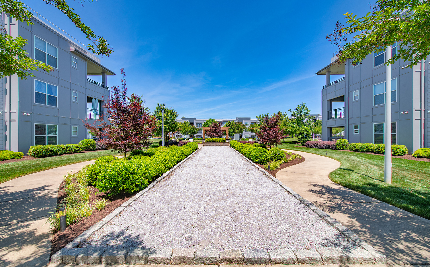 a pathway leading to an apartment building with grass and trees