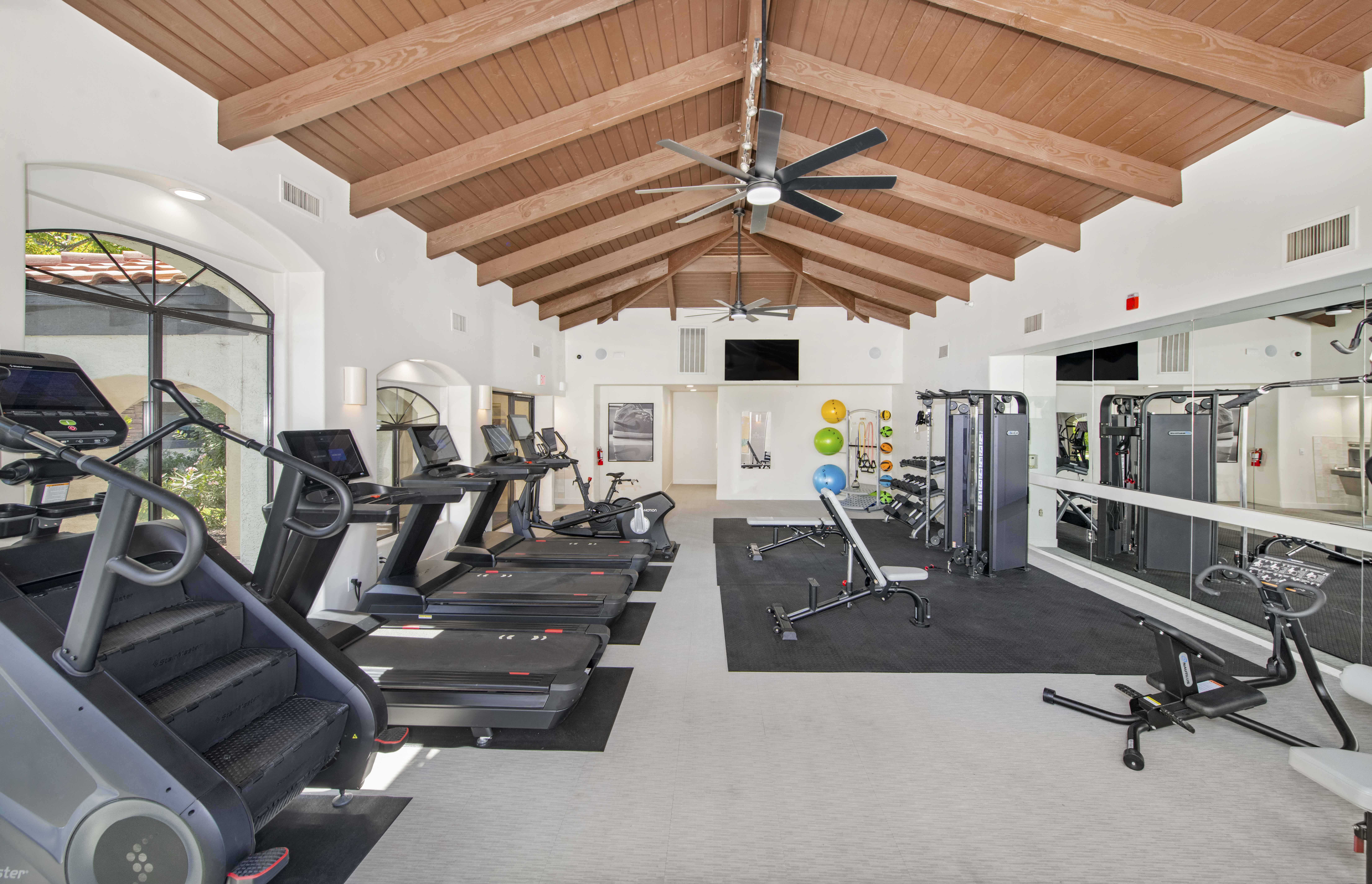 a gym with cardio equipment and a ceiling fan