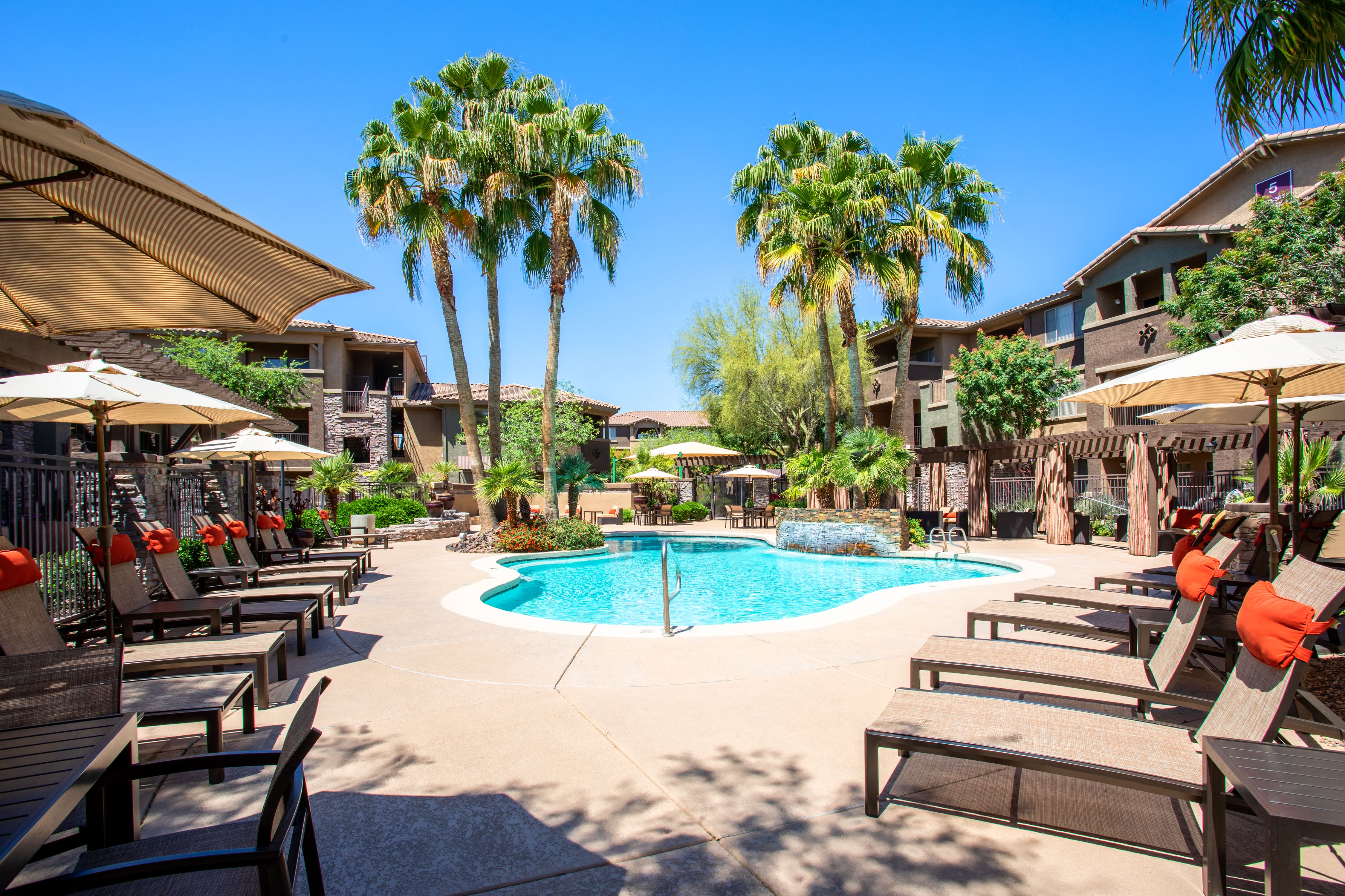 a swimming pool with tables and umbrellas at the resort with palm trees