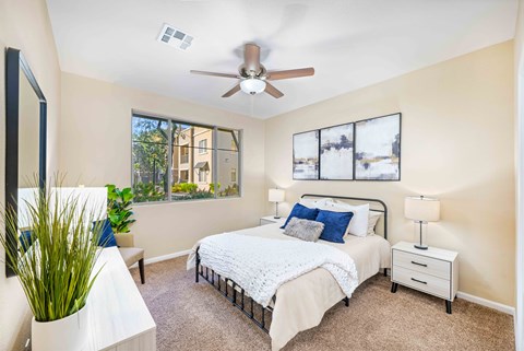 A bedroom with a large bed, a ceiling fan, and a window with a view of a building outside.