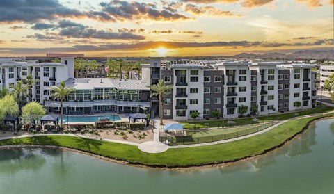 A sunset view of apartment buildings with a pool and a body of water in the foreground.