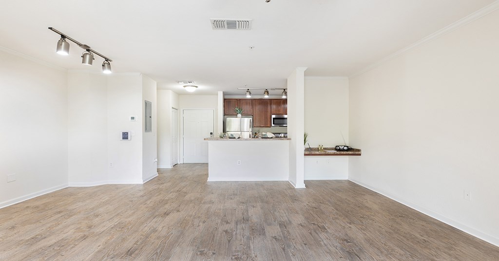 A room with a kitchen area in the background and a table with a vase on it in the foreground.