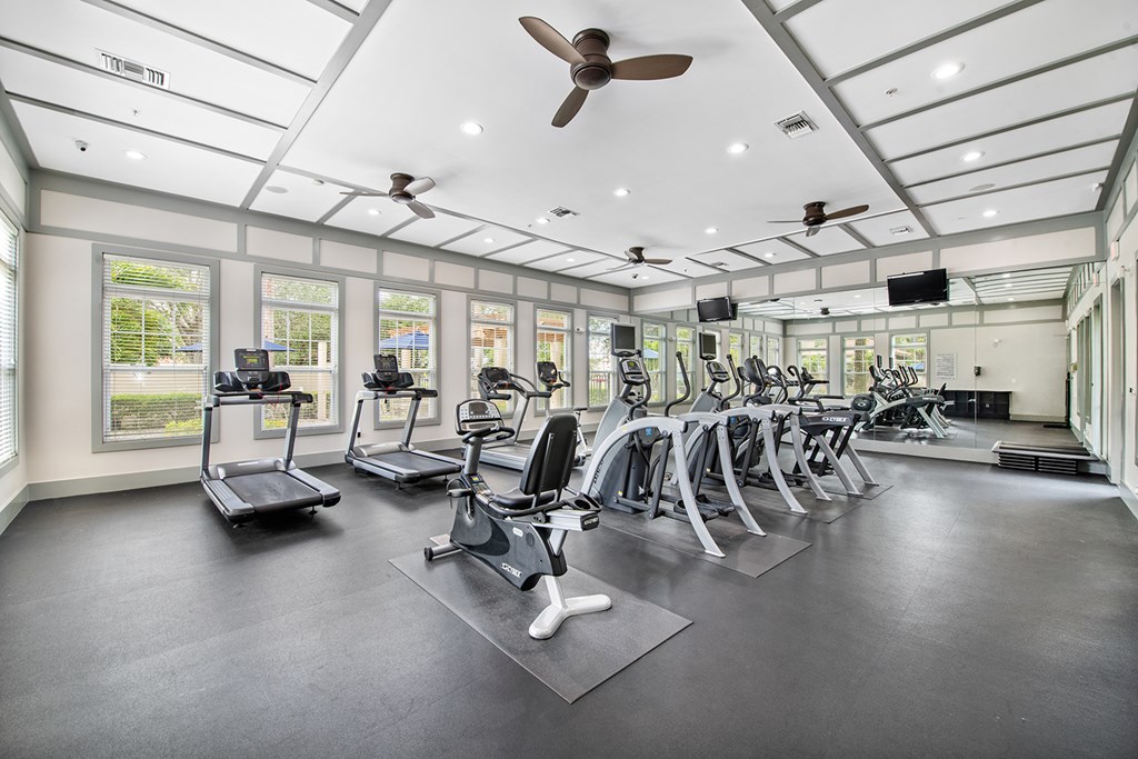 A spacious gym with treadmills, elliptical machines, and a ceiling fan.