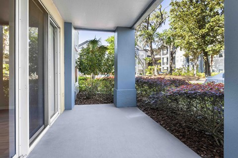 A patio with a white floor and a view of a garden and buildings.