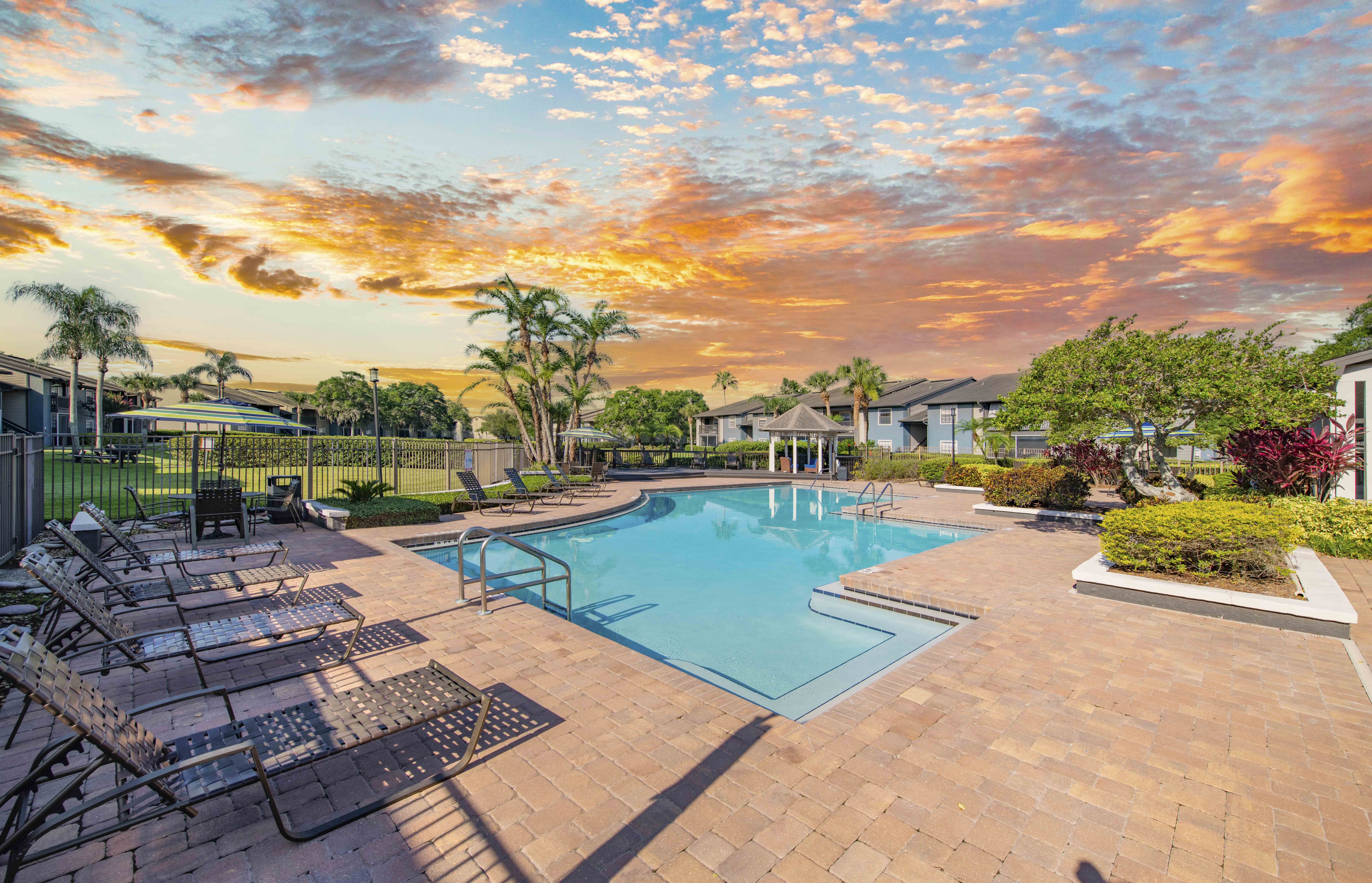a swimming pool with chairs around it at sunset