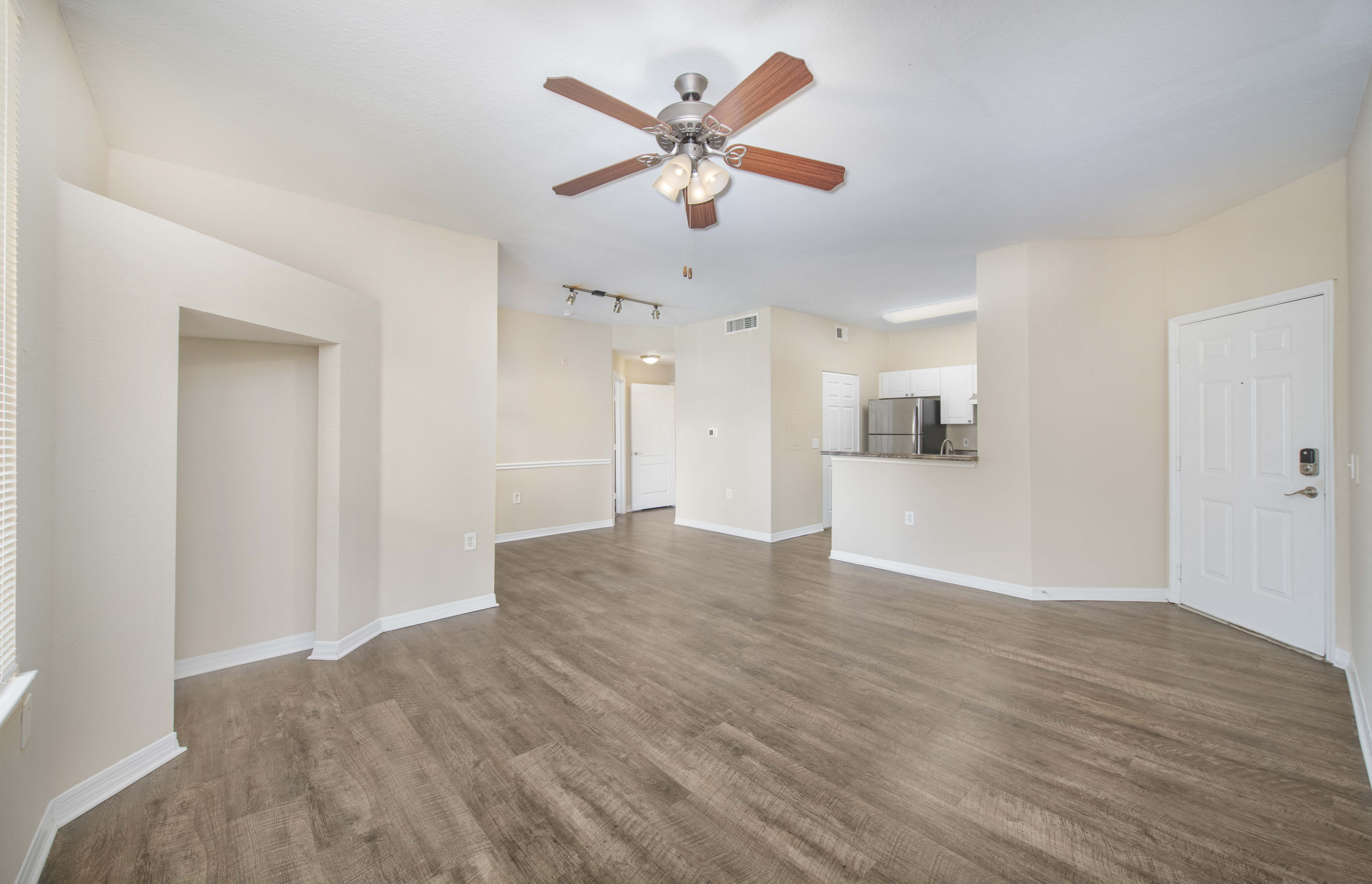 an empty living room with a ceiling fan and a kitchen