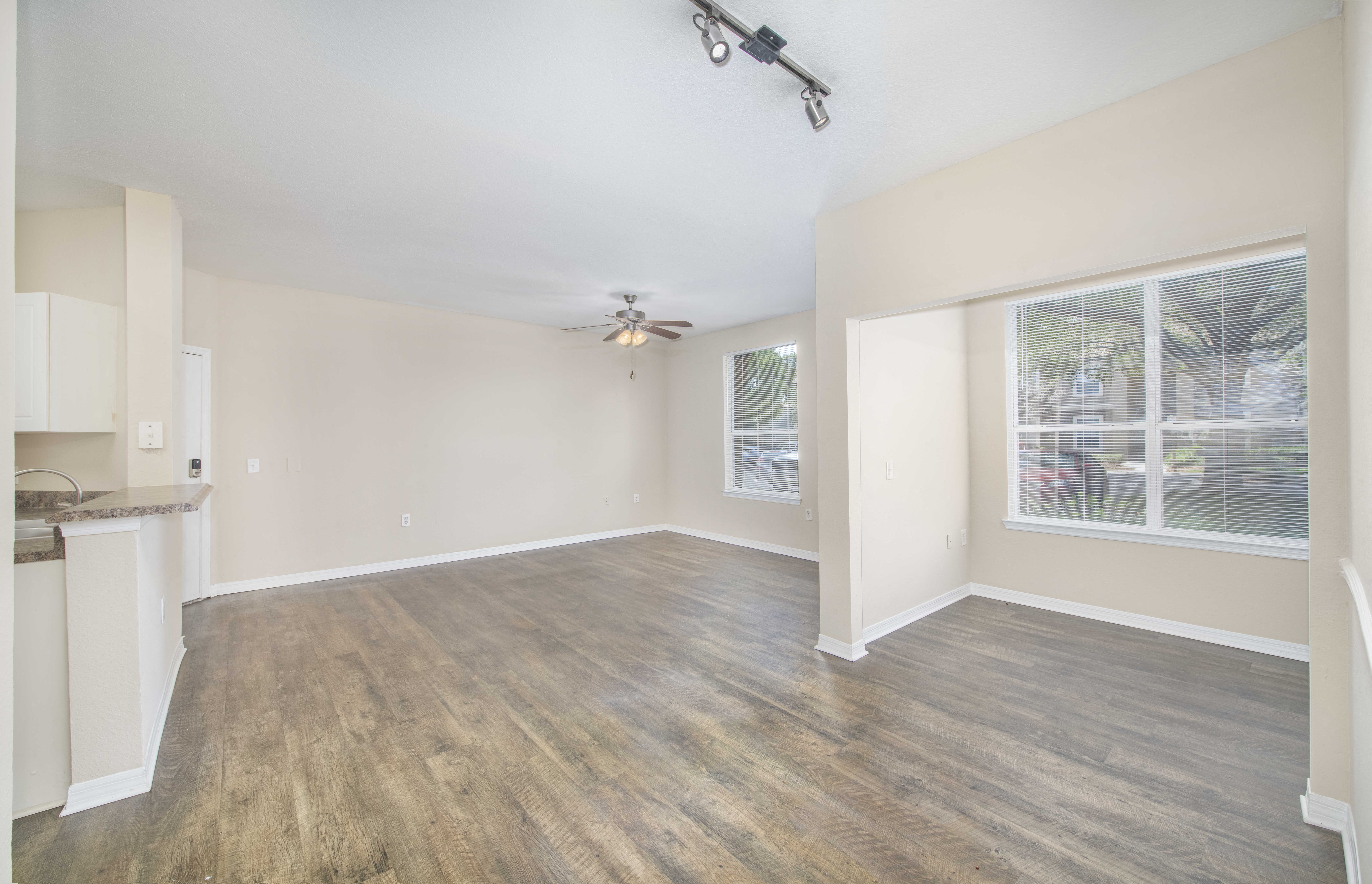 an empty living room with a kitchen and a ceiling fan