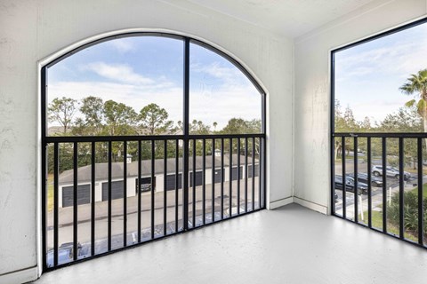 A balcony with a black railing and a view of a parking lot and trees.