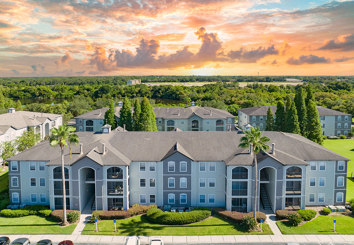 an aerial view of a building with palm trees and a sunset in the background