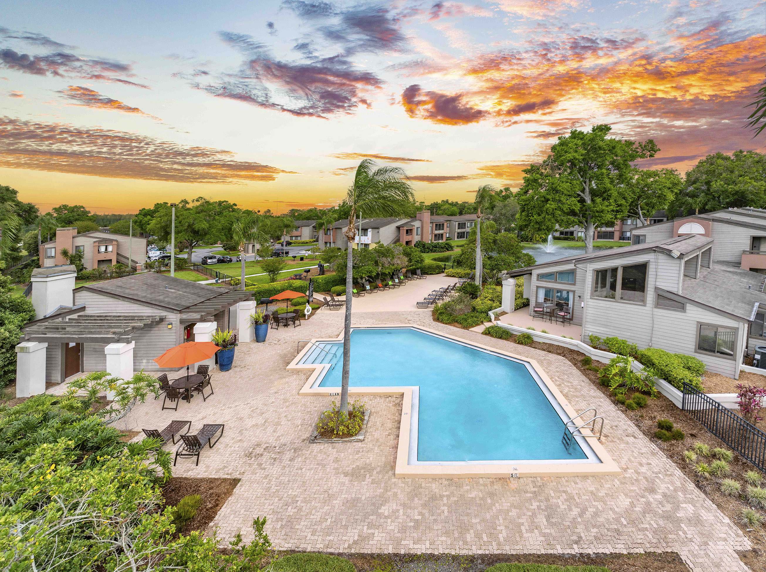 a backyard with a pool and houses with a sunset