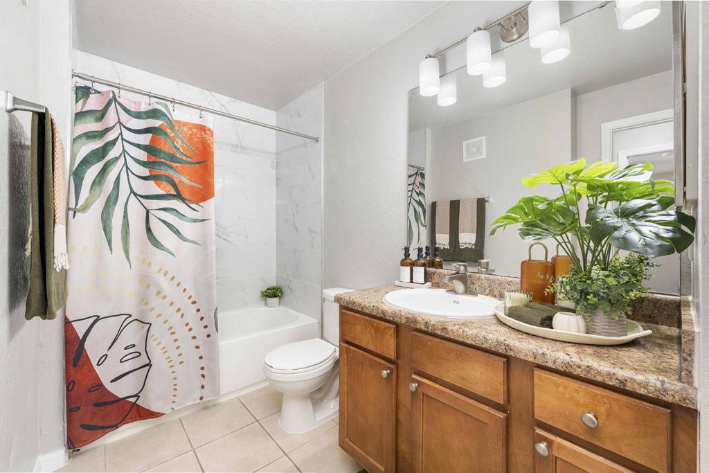 A bathroom with a white toilet, a sink, and a shower with a leafy shower curtain.
