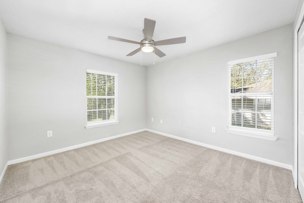A room with a ceiling fan and two windows.