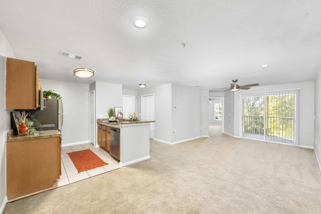A spacious living room with a kitchenette and sliding glass doors leading to a balcony.