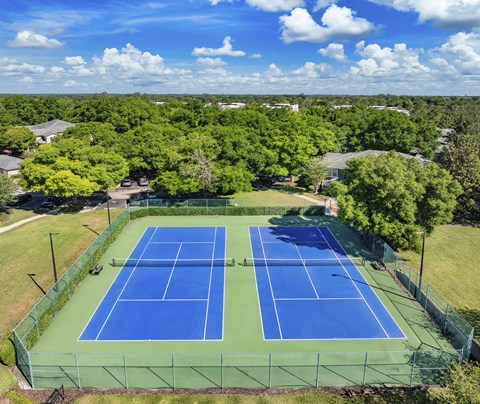 an aerial view of a tennis court with trees and houses in the background