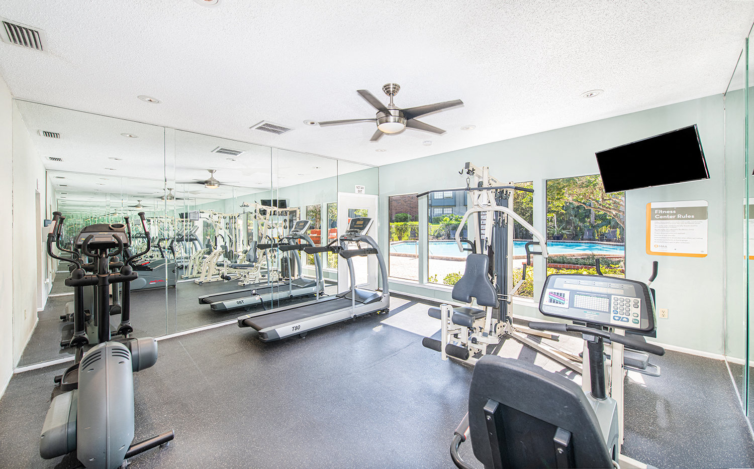 a gym with cardio machines and a ceiling fan