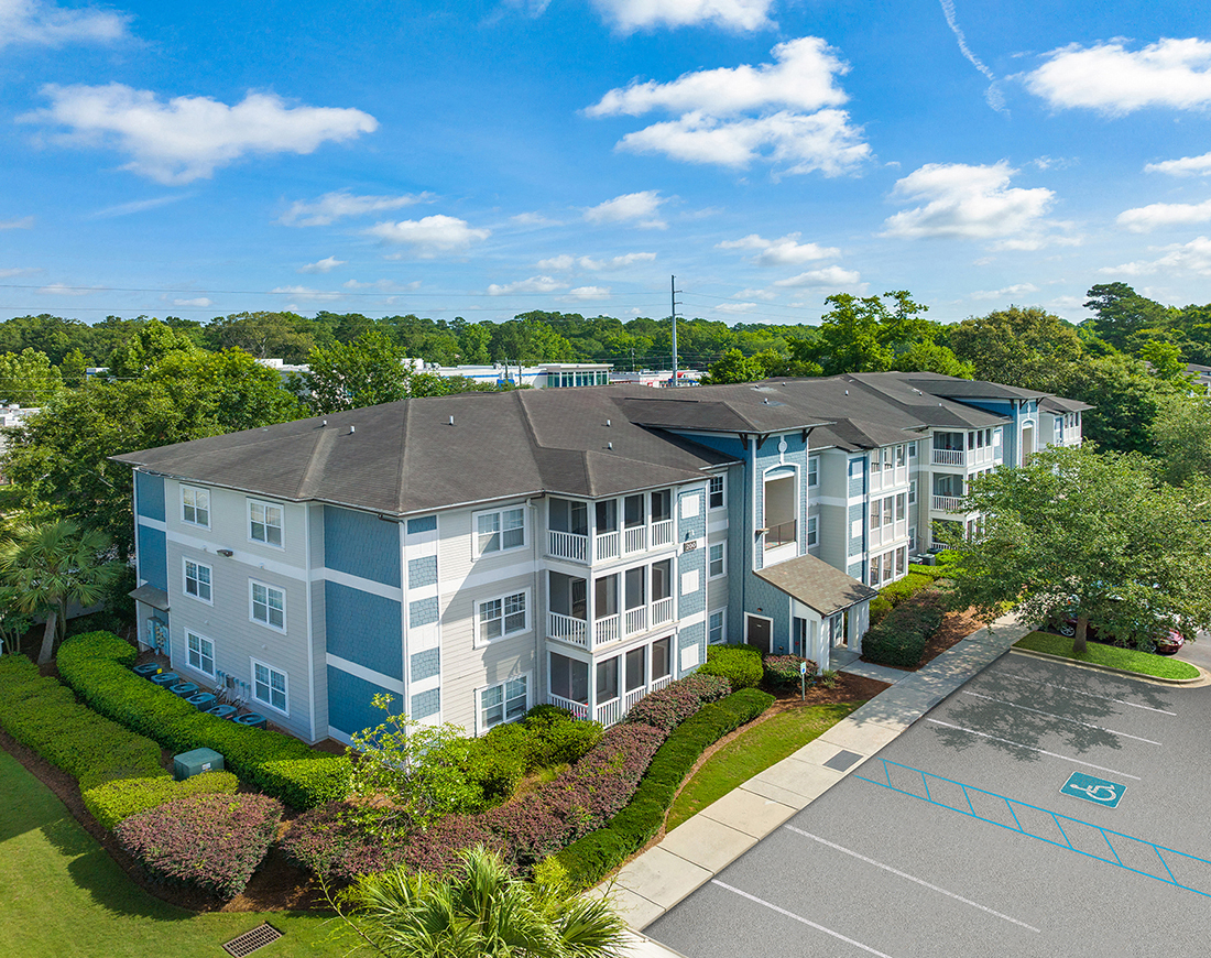 an aerial view of an apartment building with a parking lot and trees
