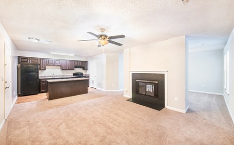 an empty living room with a fireplace and a kitchen