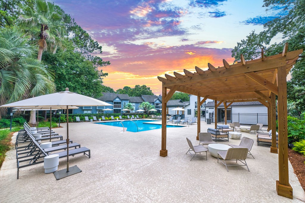 A poolside area with a wooden pergola and lounge chairs.