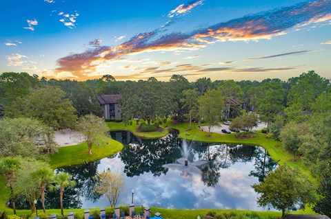 a sunset over a pond at a resort with trees and buildings