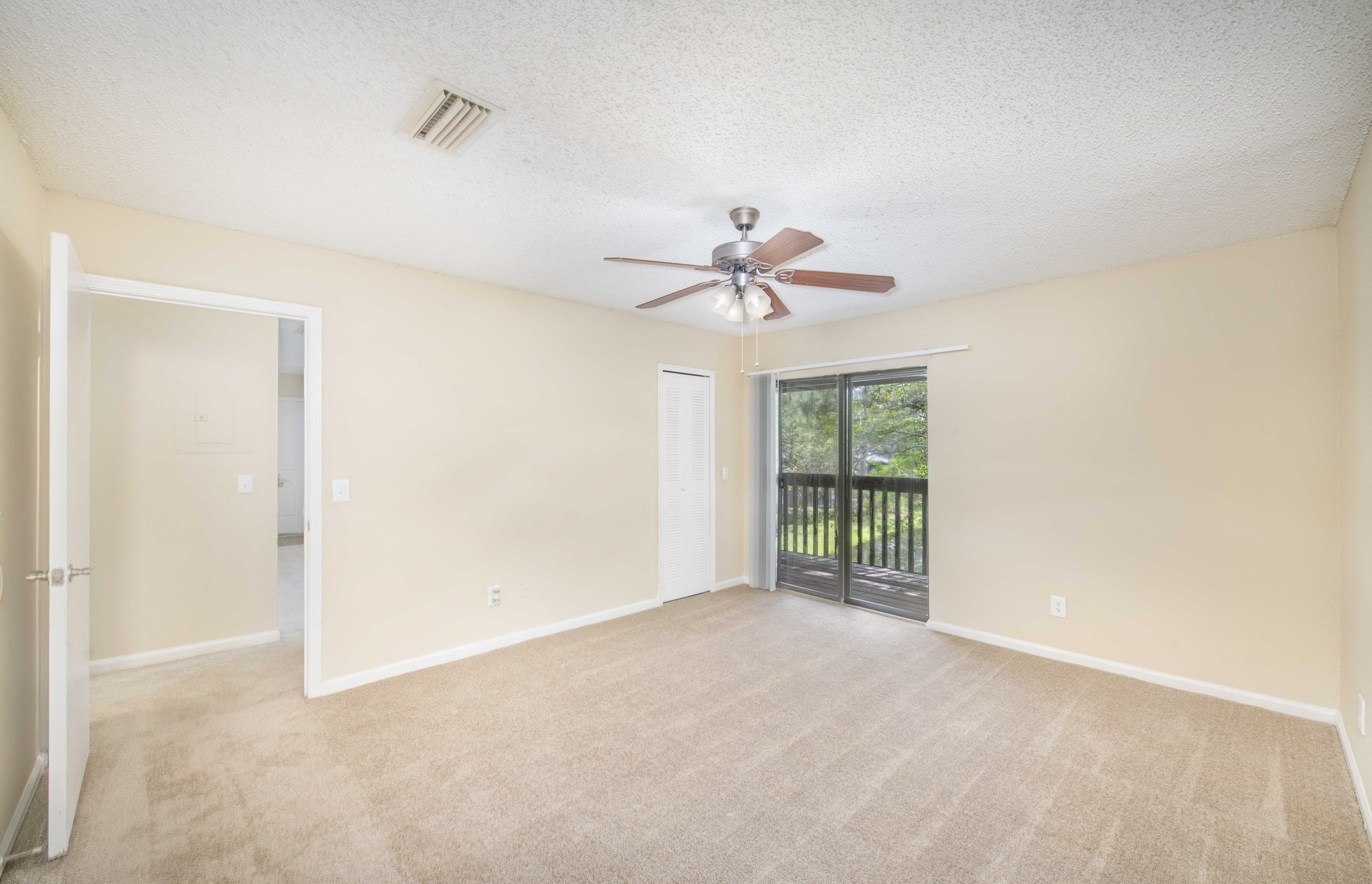 an empty living room with a ceiling fan and a door to a balcony