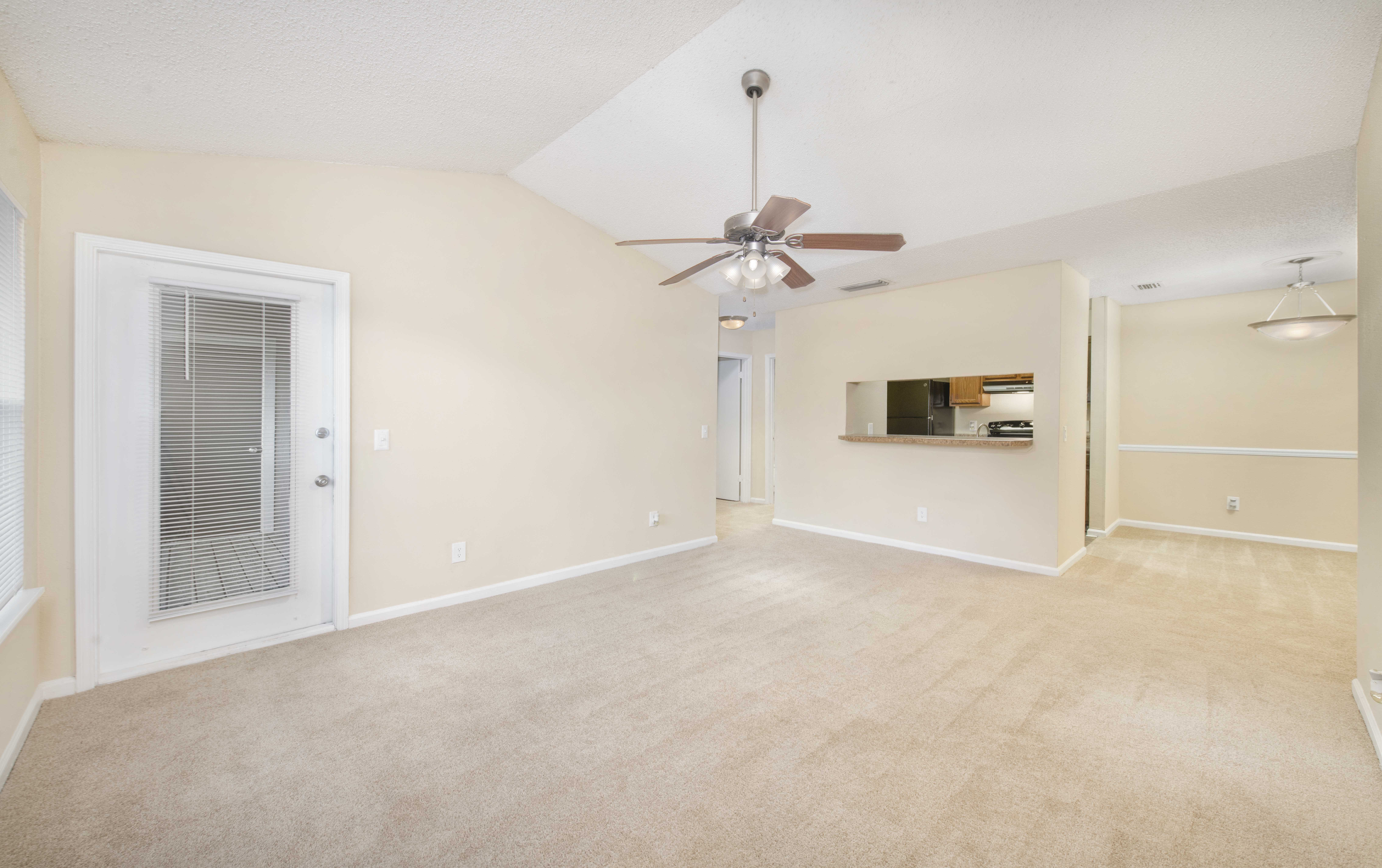 an empty living room with a ceiling fan and a door to a kitchen