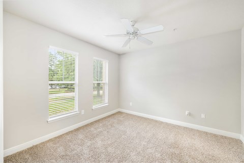 an empty room with two windows and a ceiling fan