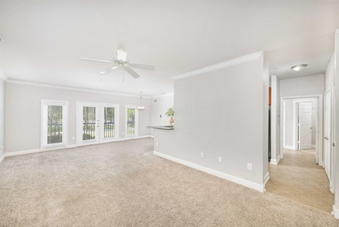 an empty living room with a ceiling fan and a hallway