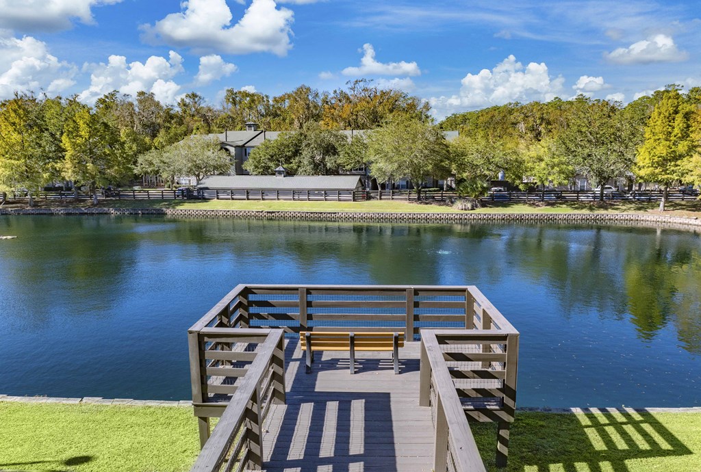 A wooden dock extends into a lake with a bench on it.
